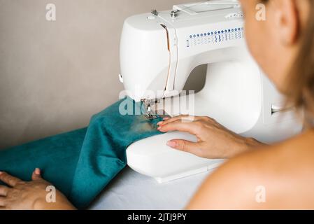 Hände in den Prozess des Nähens. Damenhänden nähen Stoff auf einer Hobby-Schreibmaschine zu Hause. Stockfoto