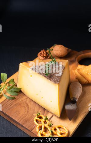 Food Concept Französischer Käse Tomme de Savoie auf Holzbrett auf schwarzem Hintergrund mit Kopierfläche Stockfoto