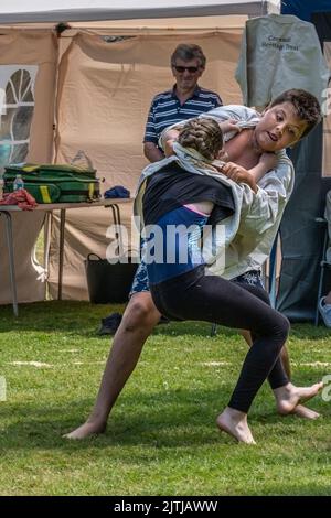 Ein junges Mädchen, das beim Grand Cornish Wrestling Tournament auf dem malerischen Dorfgrün von St. Mawgan in Pydar in Cornwa gegen einen größeren Jungen antritt Stockfoto