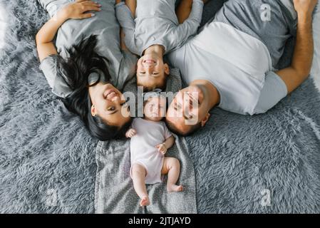 Glückliche Familie mit zwei kleinen Kindern liegen auf dem Bett und lächeln. Draufsicht Stockfoto