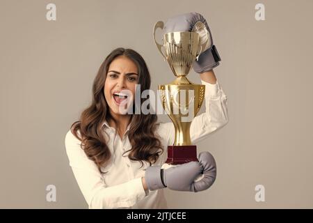 Frau in Boxhandschuhen halten Champion Siegerpokal, Trophäe. Schreiende starke junge Boxerin. Starke aggressive Geschäftsfrau Konzept. Gewinnerin weiblich Stockfoto