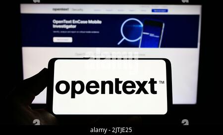 Person, die das Smartphone mit dem Logo des kanadischen Softwareunternehmens OpenText Corporation auf dem Bildschirm vor der Website hält. Konzentrieren Sie sich auf die Telefonanzeige. Stockfoto