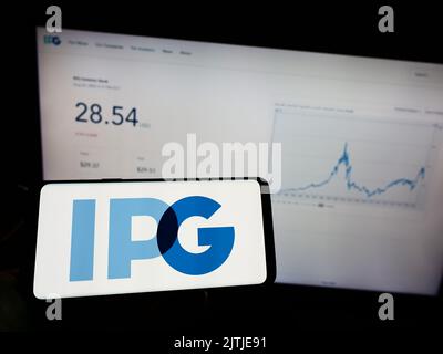 Person, die ein Mobiltelefon mit dem Logo der Interpublic Group of Companies Inc. (IPG) auf dem Bildschirm vor der Unternehmenswebseite hält. Konzentrieren Sie sich auf die Telefonanzeige. Stockfoto