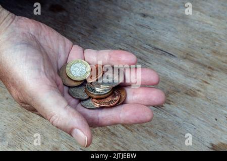 Eine ältere Hand hält britische Münzen im Wert von ein paar Pfund. Wie weit wird es sich erstrecken. Stockfoto