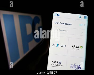 Person mit Smartphone und Website der Interpublic Group of Companies Inc. (IPG) auf dem Bildschirm vor dem Logo. Konzentrieren Sie sich auf die Mitte des Telefondisplays. Stockfoto