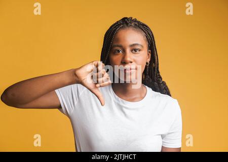 Schrecklicher Service. Porträt von unzufrieden Mädchen zeigt doppelte Daumen nach unten und Grimassen vor Ekel, Ausdruck von Missbilligung, schlechtes Feedback. Indoor-Studio auf gelbem Hintergrund gedreht Stockfoto