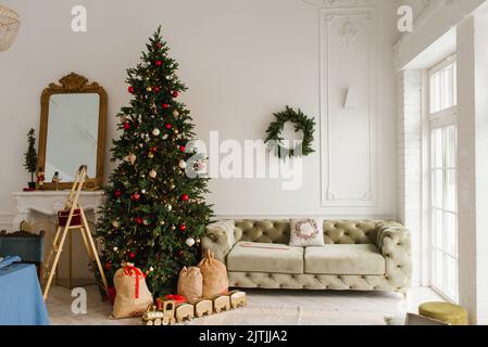 Luxuriöse Innenausstattung des Wohnzimmers im klassischen Stil. Sofa, Weihnachtsbaum mit Geschenken am Kamin Stockfoto
