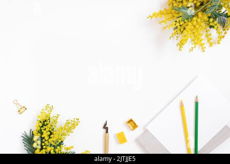 Flaches Lay des Arbeitsplatzes eines Kalligraphen-Bloggers. Ein Blatt Papier, ein Stift für Kalligraphie, Buntstifte, Blumen, Aquarellfarben auf einem weißen b Stockfoto