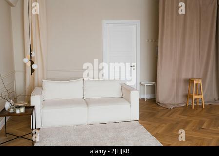 Skandinavische Einrichtung mit einem hellen Sofa auf einem Holzparkettboden, einem Beistelltisch aus Holz und beigefarbenen Wänden Stockfoto