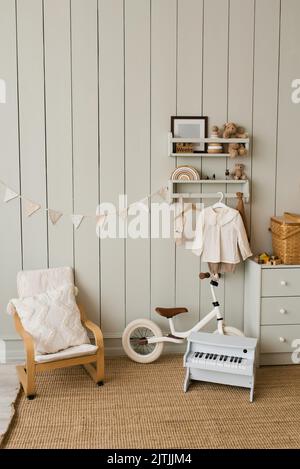 Stilvolle Komposition aus einem gemütlichen skandinavischen Interieur eines Kinderzimmers mit einem Sessel, Plüsch und Holzspielzeug, einem Rattankorb auf der Brust des Draw Stockfoto