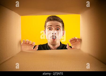 Wow. Überraschte den Mann beim Auspacken, beim Öffnen des Kartons und beim Blick nach innen mit weit geöffneten Augen. Lieferung, Überraschung, Geschenk, Wow Emotionen Konzept. Stockfoto