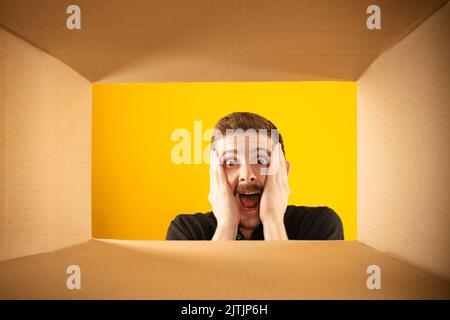 Unglaublich. Überraschte den Mann beim Auspacken, beim Öffnen des Kartons und beim Blick nach innen mit weit geöffneten Augen. Lieferung, Überraschung, Geschenk, Wow Emotionen Konzept. Stockfoto