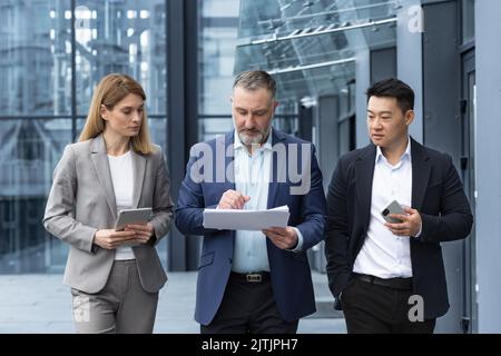 Vielfältiges Geschäftsteam drei Kollegen Mitarbeiter diskutieren Dokumente Vertrag außerhalb Büro Gebäude Geschäftsmann und Geschäftsfrau halten Rechnungen und Finanzberichte reden Stockfoto