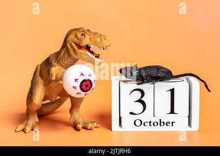 Spielzeug-Dinosaurier Tyrannosaurus mit Auge in den Pfoten, Kalenderdatum 31 Oktober isoliert auf orangefarbenem Hintergrund Feiertag Grußkarte Happy Halloween day c Stockfoto