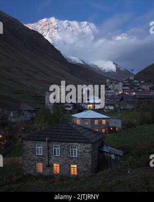 Nachtansicht von Steinhäusern und mittelalterlichen Türmen in der Gemeinde Ushguli und dem schneebedeckten Gipfel des Mount Shkhara in Svaneti, Georgien Stockfoto