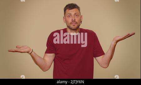 Ich weiß nicht, was ich sagen soll. Verwirrter, hübscher junger Mann, der sich über zweideutige Fragen verlegen fühlt, Zweifel hat, keine Ahnung hat, ahnungslos und unsicher ist. Erwachsene stilvollen Kerl auf beige Studio Hintergrund Stockfoto