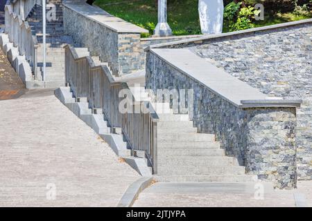 Granitstufen in einem modernen Stadtpark mit Edelstahlgeländern an einem sonnigen Tag vor dem Hintergrund der Landschaftsgestaltung. Stockfoto