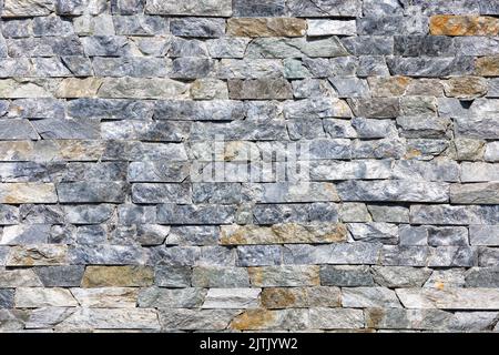 Struktur und Hintergrund einer Steinwand aus asymmetrischen, natürlichen grauen Granitfliesen, die horizontal ausgelegt sind. Durch Sonnenlicht beleuchtete Textur. Stockfoto
