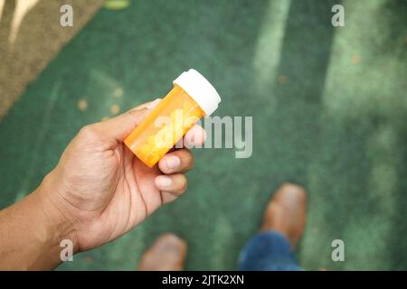Junger Mann hält einen Behälter mit Medikamentenpillen in der Hand Stockfoto