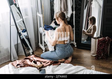 Schrank organisieren, Schrank entkleiden. Junge Frau entrümpelt Kleiderschrank und Wahl Kleidung im Schlafzimmer Stockfoto