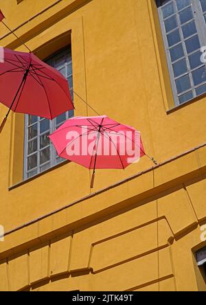 Gelbe Wand und rosa Regenschirm über der Straße Stockfoto