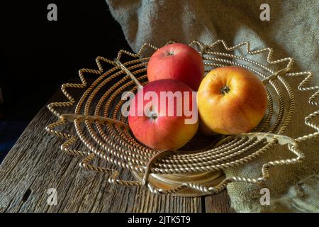 Äpfel auf dunklem Hintergrund mit Sackleinen. Reife Früchte auf dem Tisch auf einem alten Teller Stockfoto