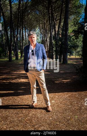 Der wunderschöne blauäugige Mann trägt eine blaue Jacke und eine Bedge-Hose. Der Geschäftsmann arbeitet im Park im Freien. Stockfoto