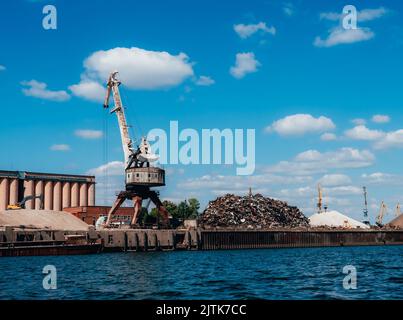 Hafenkrane an der Wolga, Russland. Infrastruktur für den Güterverkehr auf Flüssen. Verladung von Metallschrott auf den Lastkahn. Stockfoto