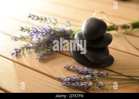 Balance- und Gesundheitskonzept mit Haufen schwarzer Steine auf Holz und Blütenlavendelspikes. Ansicht von oben. Horizontale Zusammensetzung. Stockfoto