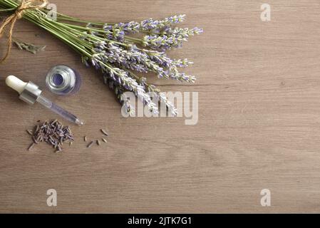 Flasche mit Tropf mit Lavendelessenz auf Holztisch mit Blumenstrauß von blühenden Lavendel. Draufsicht. Stockfoto