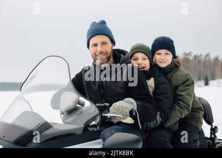 Porträt eines lächelnden Mannes, der im Winter mit Jungen auf dem Schneemobil unterwegs ist Stockfoto