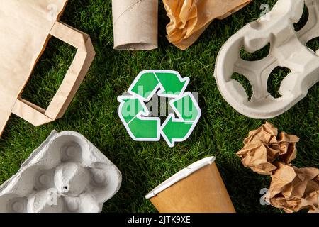 Grünes Recycling-Zeichen und Papierabfall auf Gras Stockfoto