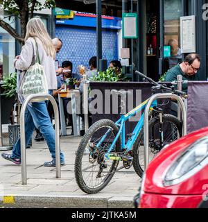 Kingston-upon-Thames, London, Großbritannien, August 29 2022, Menschen, die an Einem Restaurant vor dem Sitzbereich mit geparkten Fahrrädern auf dem Bürgersteig vorbeigehen Stockfoto