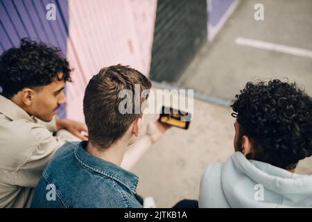 Junger Mann, der im Freien sitzt und Smartphone mit Freunden teilt Stockfoto