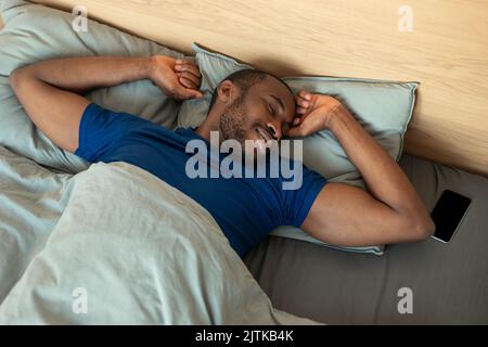 Afroamerikanischer Mann Schläft Gut Und Streckt Arme Im Schlafzimmer Stockfoto