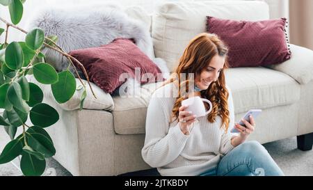 Frau Freizeit gemütlich Hause Tasse browsing Smartphone Stockfoto