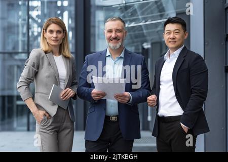 Erfolgreiche reifes Geschäftsteam Mann und Frau Geschäftsleute in Geschäftsanzügen lächeln und schauen vor dem Bürogebäude auf die Kamera und spezialisierte Investoren Team lächeln und glücklich Stockfoto