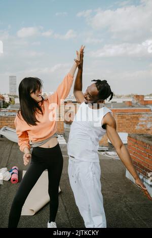 Fröhliche Frau, die einem Freund auf dem Dach einen hohen Fünftel gab Stockfoto