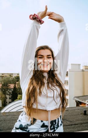 Porträt einer lächelnden Frau mit erhobenen Armen, die auf dem Dach Yoga praktiziert Stockfoto