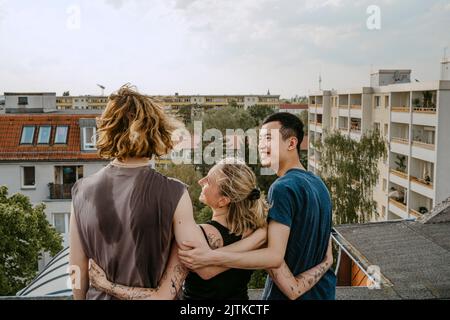 Glückliche männliche und weibliche Freunde stehen mit den Armen auf dem Dach Stockfoto
