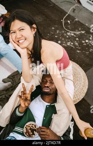 Porträt einer glücklichen jungen Frau mit einem männlichen Freund, der während einer Dachparty das Friedenszeichen gestikuliert Stockfoto