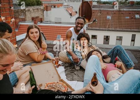 Glückliche männliche und weibliche Freunde mit Pizza genießen Party auf dem Dach Stockfoto