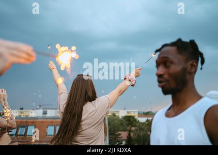 Rückansicht einer Frau mit erhobenen Armen und beleuchteten Wunderkerzen am Himmel Stockfoto