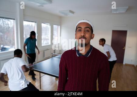 Porträt eines Mannes, der im Spielzimmer steht, während Freunde im Hintergrund Tischtennis spielen Stockfoto