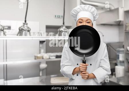 Die Köchin guckt hinter der Bratpfanne heraus Stockfoto