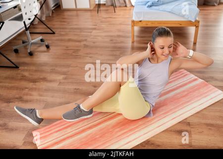 Fröhliches Teenager-Mädchen, das zu Hause auf einer Yogamatte trainiert Stockfoto