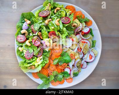 Bunte Powersalatplatte mit grünem Salat, Karottenscheiben, Tomaten, Zwiebeln, Nüssen, Rettich Kartoffelsalat, Gewürze und Zitronenmelisse Blätter Draufsicht. Stockfoto
