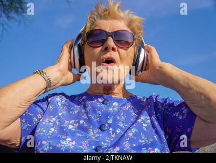 Porträt einer Rentnerin mit Sonnenbrille und Kopfhörern, die Musik hören Stockfoto