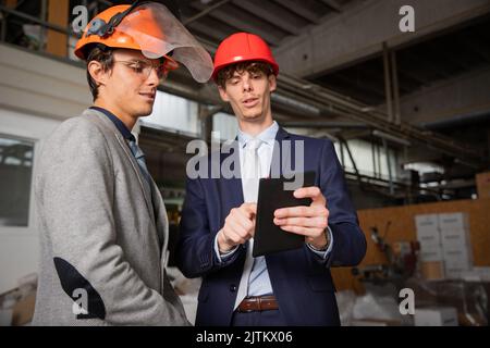 Zwei Ingenieure diskutieren im Werk mit einem Tablet über ein Projekt Stockfoto