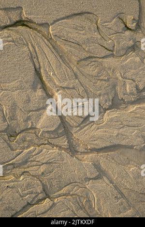 Nahaufnahme der Sandstrandwasserkanale bei Ebbe, die Spuren zeigen, wo das Wasser zurück ins Meer gelaufen ist Stockfoto